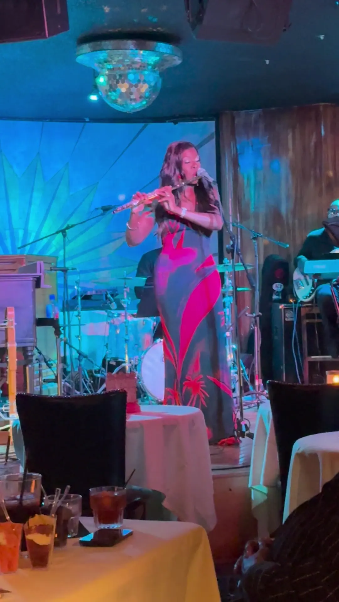 A flutist in a floor-length gown performs with a band for seated dinner guests