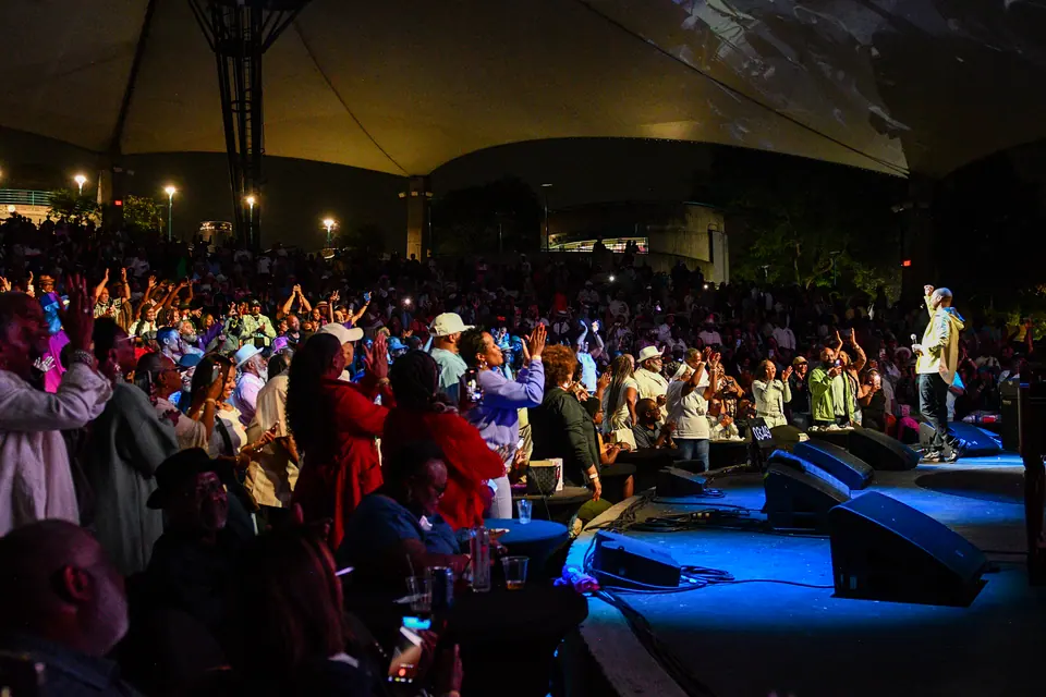 A full amphitheatre crowd with hands raised at night
